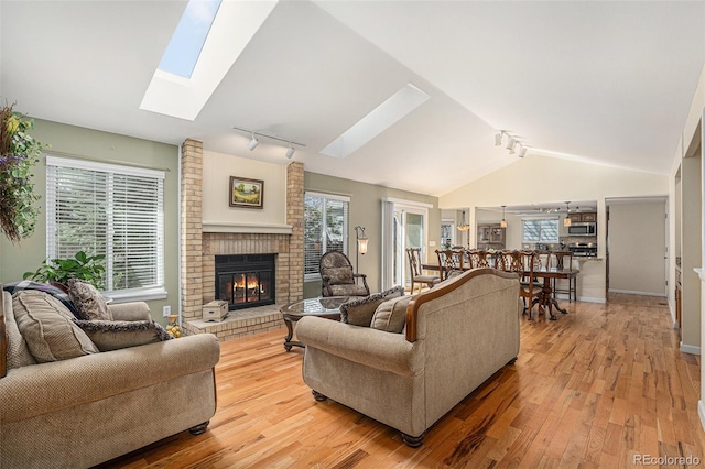 living area with lofted ceiling with skylight, light wood-style flooring, a brick fireplace, and a wealth of natural light