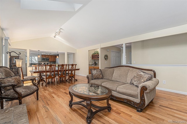 living area with baseboards, light wood finished floors, rail lighting, and vaulted ceiling