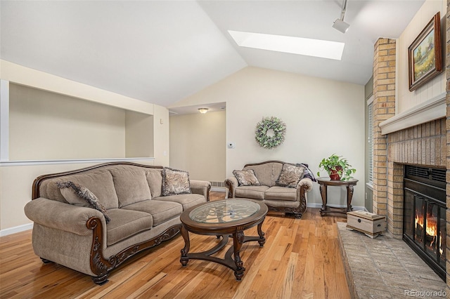 living area featuring lofted ceiling with skylight, a fireplace, light wood-style floors, and baseboards