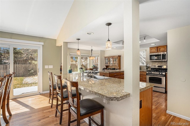 kitchen featuring brown cabinetry, light wood finished floors, a sink, appliances with stainless steel finishes, and tasteful backsplash