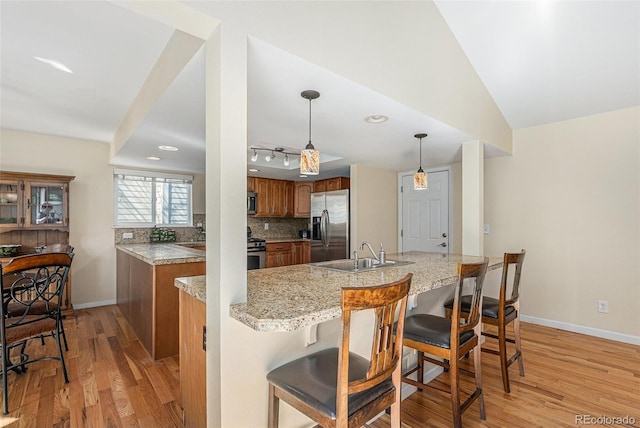 kitchen with backsplash, brown cabinets, light wood-style flooring, stainless steel appliances, and a sink