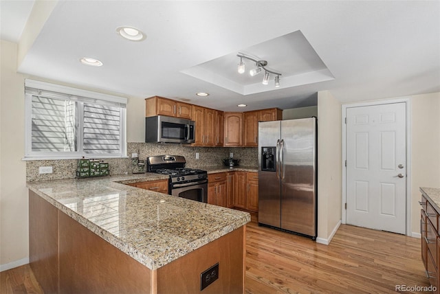 kitchen with stainless steel appliances, a raised ceiling, light wood-style flooring, and decorative backsplash