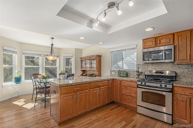 kitchen featuring brown cabinets, a peninsula, appliances with stainless steel finishes, a raised ceiling, and light wood-type flooring