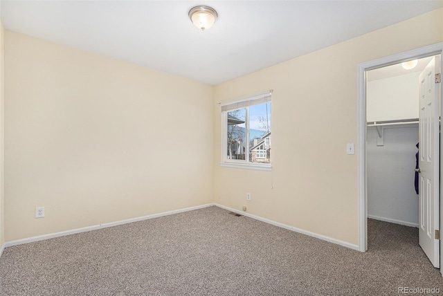 unfurnished bedroom featuring a closet, carpet flooring, a walk in closet, and baseboards