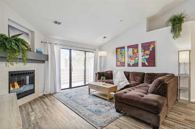 living room featuring a tile fireplace, vaulted ceiling, and wood-type flooring