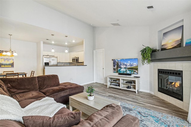 living room featuring a tile fireplace, lofted ceiling, wood-type flooring, and an inviting chandelier