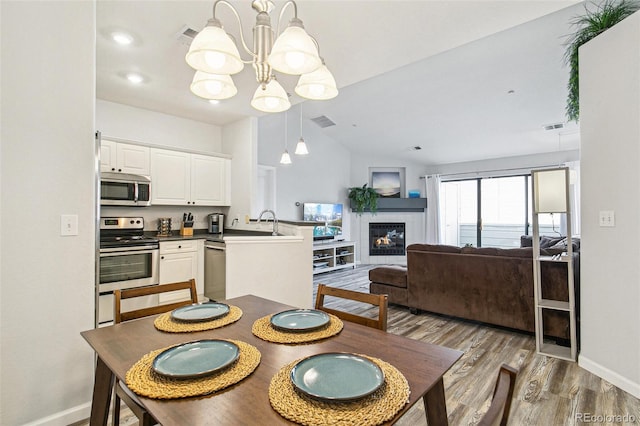 dining area with sink, a chandelier, vaulted ceiling, dark hardwood / wood-style floors, and a tiled fireplace