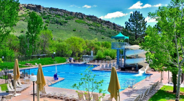 view of pool featuring a water slide, a mountain view, and a patio area