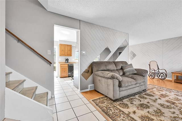 living room with light tile patterned floors, visible vents, a textured ceiling, and stairs