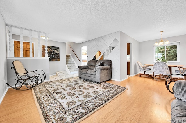 living area featuring an accent wall, stairway, wood finished floors, a notable chandelier, and a textured ceiling