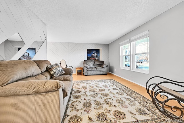 living room with a textured ceiling, wood finished floors, wooden walls, baseboards, and an accent wall