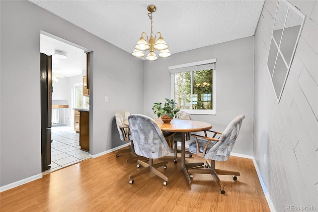 dining area with a notable chandelier, baseboards, light wood-type flooring, and a textured ceiling