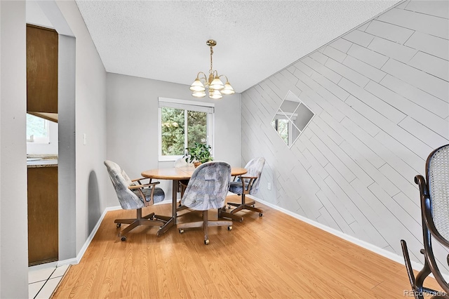 dining space with a notable chandelier, a textured ceiling, an accent wall, and light wood-style floors