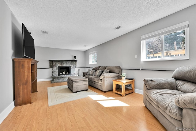 living area with a stone fireplace, light wood-style floors, visible vents, and baseboards