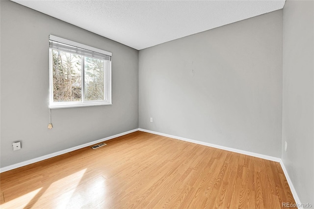 spare room featuring a textured ceiling, wood finished floors, visible vents, and baseboards