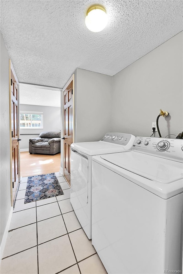 washroom featuring a textured ceiling, laundry area, light tile patterned floors, and washer and clothes dryer