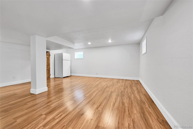 below grade area featuring light wood finished floors, baseboards, and freestanding refrigerator