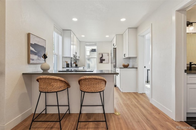 kitchen with dark countertops, white cabinets, a kitchen breakfast bar, light wood-type flooring, and a peninsula