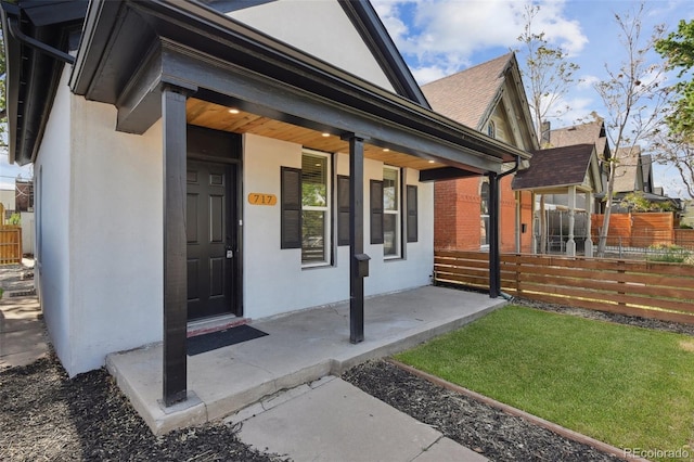 view of exterior entry featuring fence, stucco siding, and covered porch