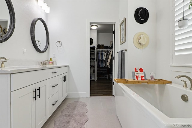 bathroom featuring a bathing tub, baseboards, tile patterned flooring, vanity, and a spacious closet