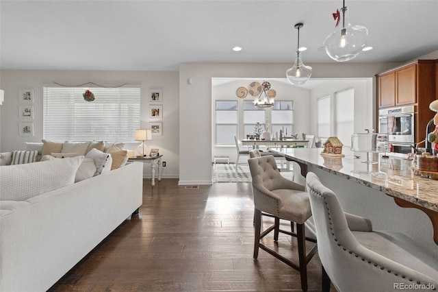 interior space with light stone countertops, dark hardwood / wood-style flooring, double oven, pendant lighting, and a kitchen bar