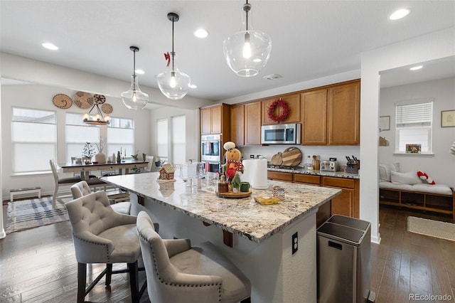 kitchen with dark wood-type flooring, a center island with sink, stainless steel appliances, and decorative light fixtures