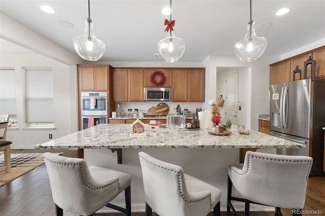 kitchen featuring a large island with sink, a kitchen breakfast bar, dark hardwood / wood-style floors, decorative light fixtures, and stainless steel appliances