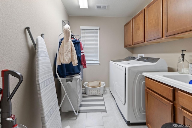 laundry room featuring washing machine and clothes dryer, light tile patterned floors, and cabinets