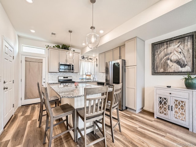 kitchen featuring decorative light fixtures, a center island, appliances with stainless steel finishes, light stone countertops, and decorative backsplash