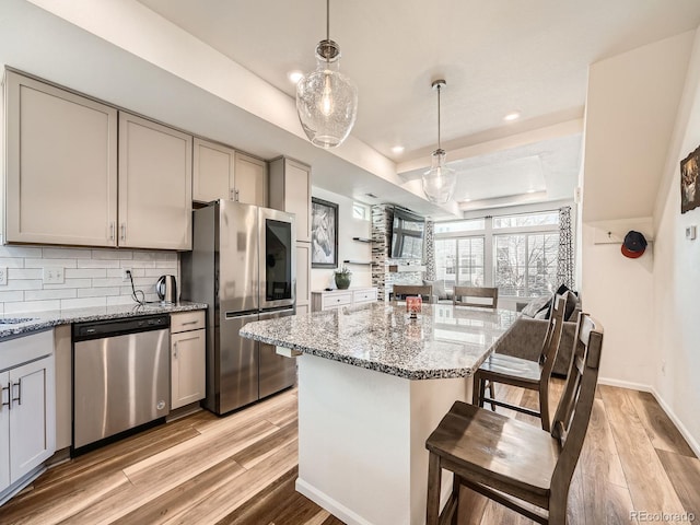 kitchen featuring gray cabinetry, a tray ceiling, pendant lighting, stainless steel appliances, and light stone countertops