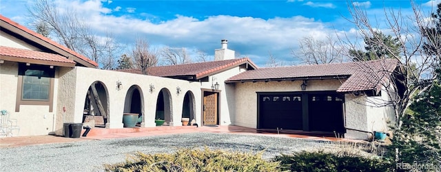 view of front of home with a tile roof, a chimney, an attached garage, and stucco siding