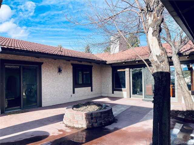 rear view of property featuring a patio area, a tiled roof, and stucco siding