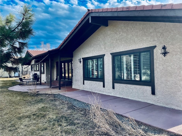 view of side of home featuring a patio, a yard, and stucco siding