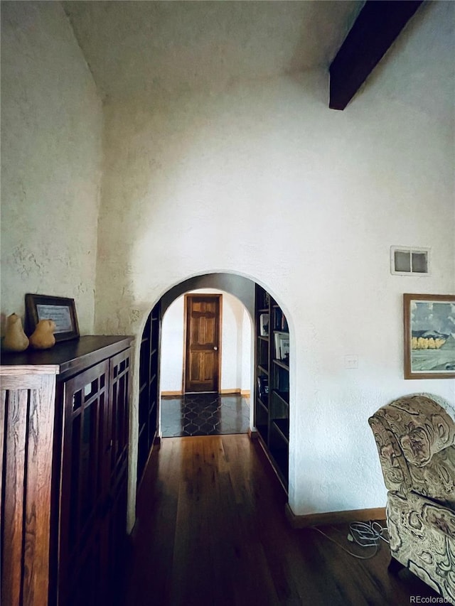 entrance foyer featuring baseboards, visible vents, arched walkways, dark wood-type flooring, and beam ceiling