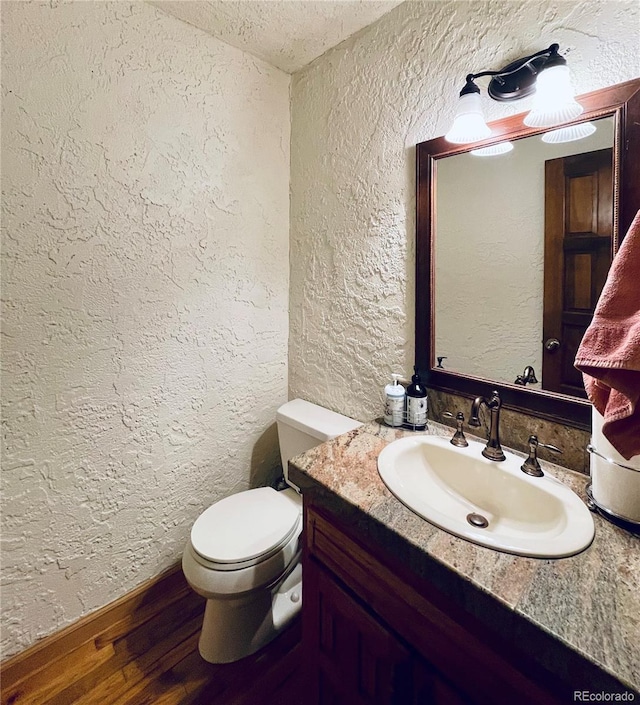 bathroom with a textured wall, vanity, toilet, and wood finished floors