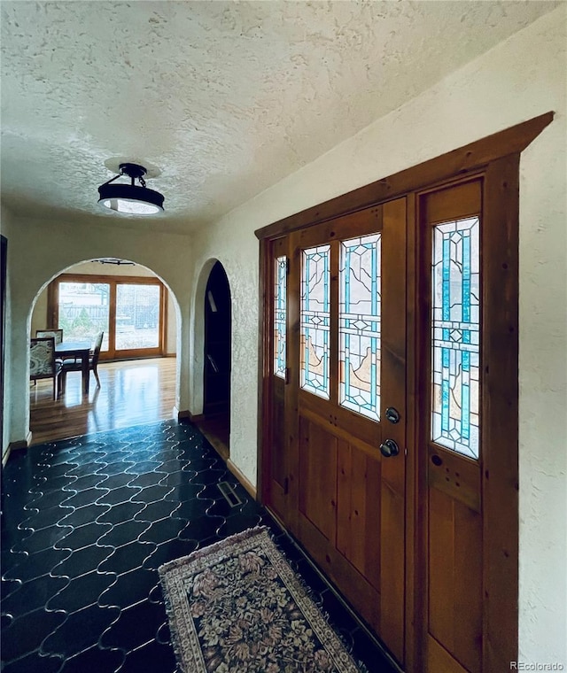 entrance foyer featuring arched walkways, a textured wall, and a textured ceiling