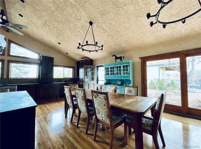 dining area with lofted ceiling, a textured ceiling, wood finished floors, and a chandelier