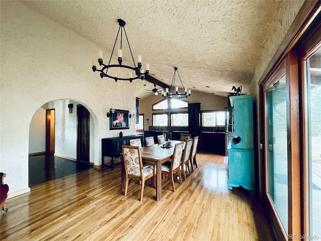 dining room with lofted ceiling, arched walkways, a chandelier, and light wood-style flooring