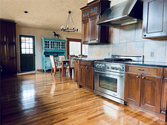 kitchen with wall chimney exhaust hood, light wood-style flooring, high end range, and decorative light fixtures