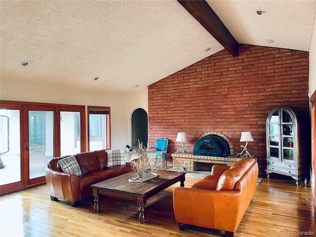 living room with a healthy amount of sunlight, a fireplace, vaulted ceiling with beams, and light wood finished floors