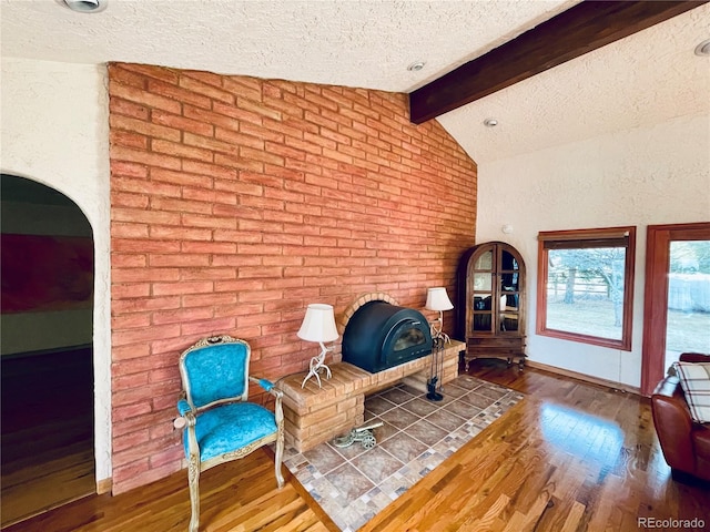 sitting room with a wood stove, lofted ceiling with beams, a textured ceiling, and wood finished floors