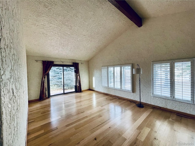 empty room with light wood finished floors, a textured ceiling, high vaulted ceiling, beamed ceiling, and baseboards