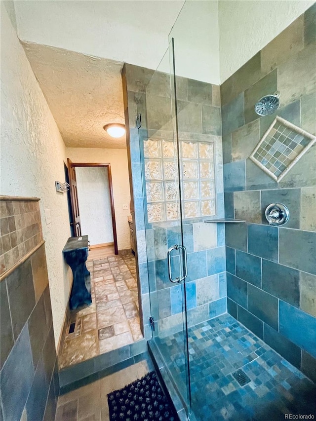 full bathroom with a textured ceiling, a textured wall, and a stall shower