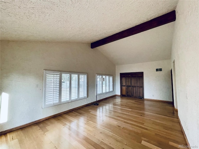 unfurnished living room featuring a textured ceiling, wood finished floors, visible vents, baseboards, and beam ceiling