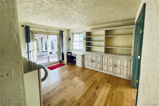 unfurnished living room featuring a textured wall, built in study area, and light wood-style flooring