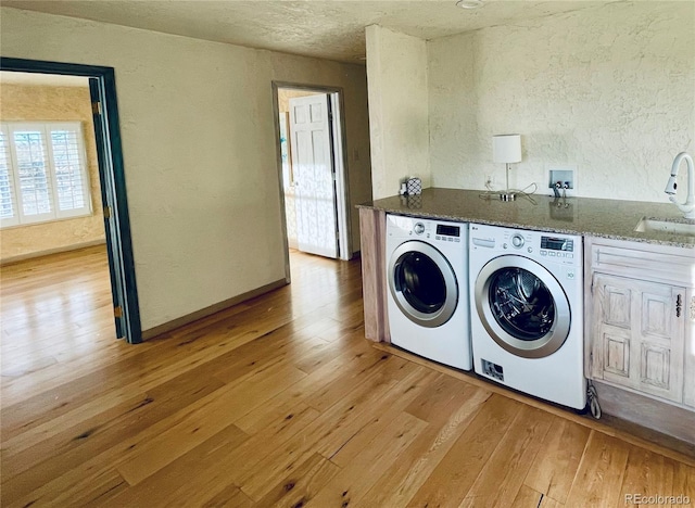 laundry area with cabinet space, a textured wall, light wood-style floors, a sink, and separate washer and dryer