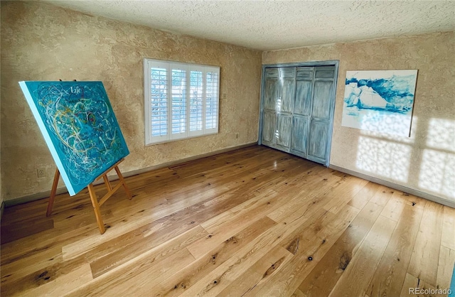 unfurnished bedroom featuring hardwood / wood-style flooring, a closet, baseboards, and a textured ceiling