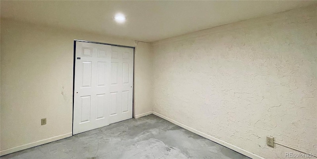 unfurnished bedroom with concrete flooring, a textured wall, and baseboards