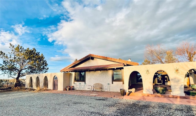 back of property with fence, a tile roof, stucco siding, a chimney, and a patio area