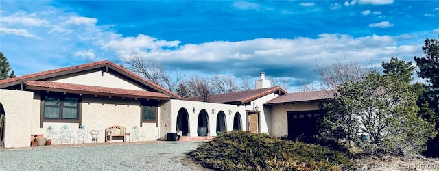 view of front of home featuring a chimney, an attached garage, and stucco siding